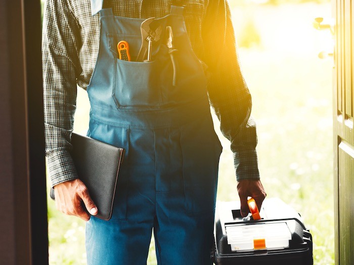 Man in overalls holding repair tools.